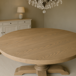 Close-up of round solid ash dining table top by Rustic 9, highlighting natural wood grain, beveled edge, and smooth artisan finish beneath a crystal chandelier.
